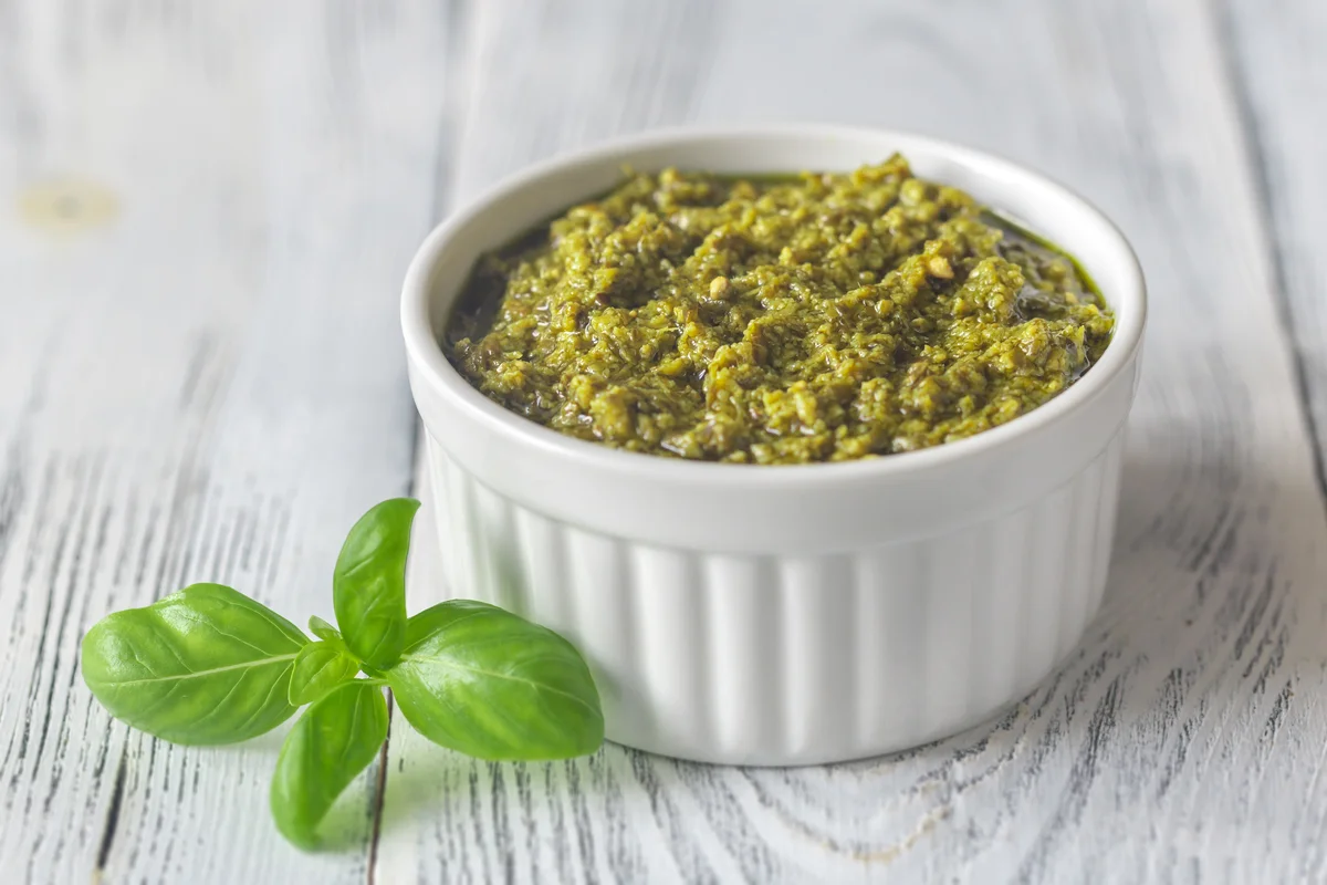 Homemade pistachio paste recipe in a glass jar, with shelled pistachios scattered around.